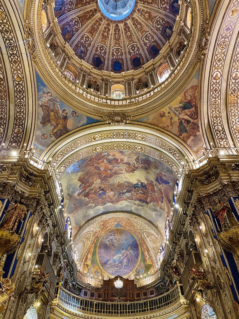 Ornate interior of a domed cathedral with intricate gold detailing, vibrant frescoes, and elaborate features—one of the hidden gems of Granada—viewed from below, inviting awe as you gaze up toward the magnificent dome.