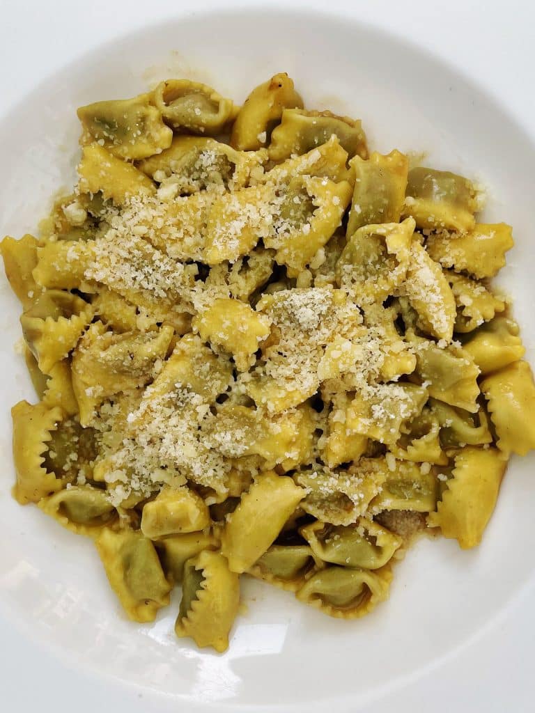 A white plate filled yellow pasta, Agnolotti del Plin topped with a generous sprinkle of grated cheese—just one of many reasons to visit Turin for its delicious cuisine.