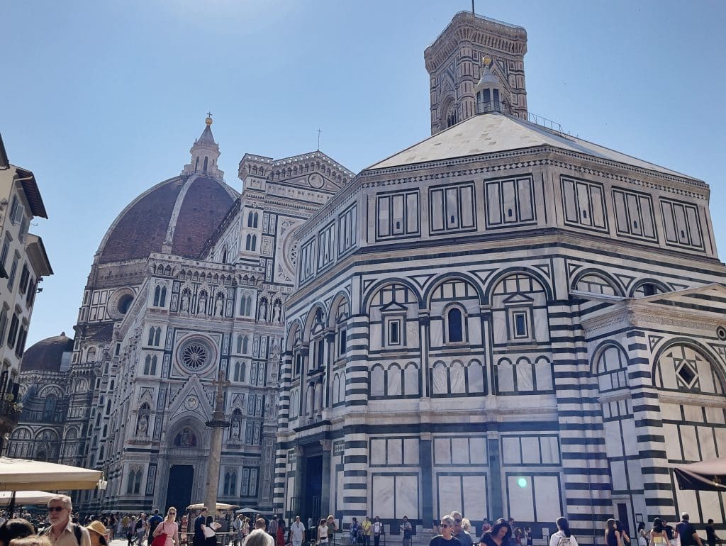The image shows the magnificent Florence Cathedral, or Duomo, with its iconic red-tiled dome and the Baptistery of St. John in the foreground. The ornate architecture features captivating geometric patterns. For first-time visitors, here are some Florence Duomo tips to enhance your experience.
