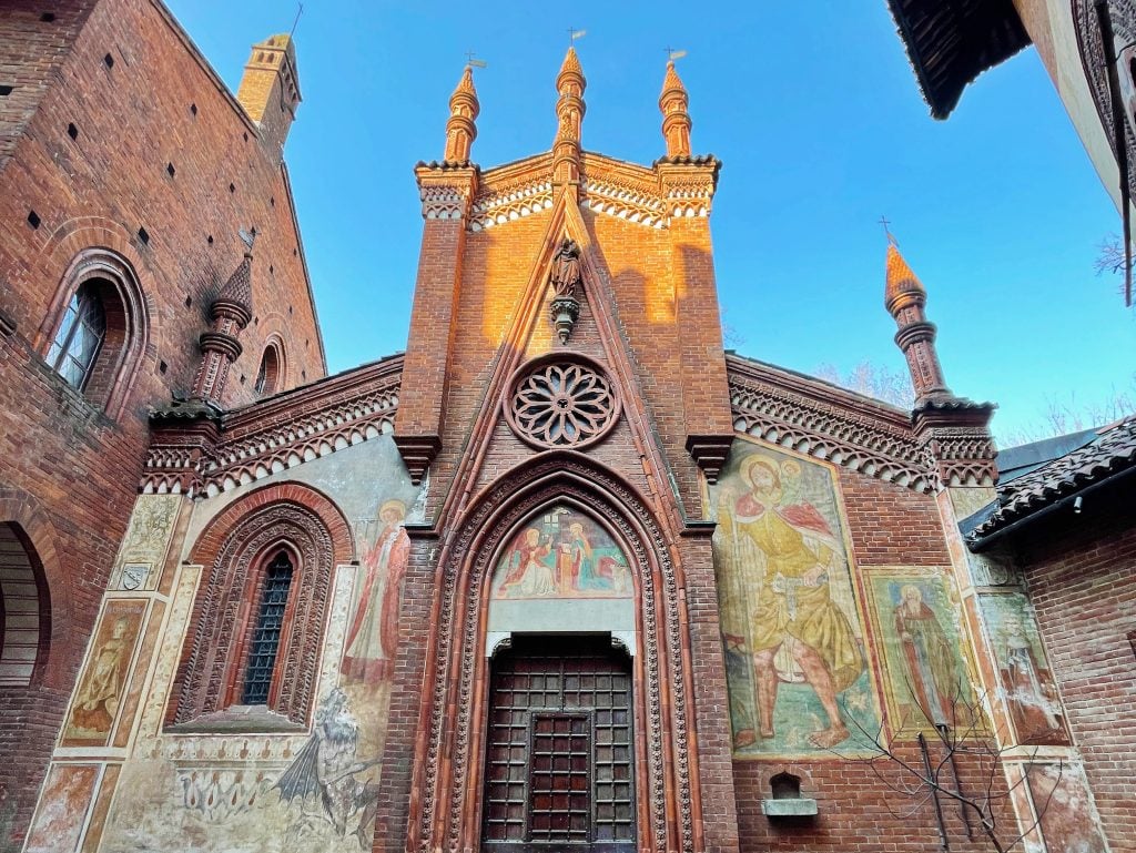 Red brick Gothic church facade with pointed arches, rose window, and spires. Large religious frescoes and murals decorate the walls. This is a hidden gem within the Parco del Valentino, and a really fun place to visit.