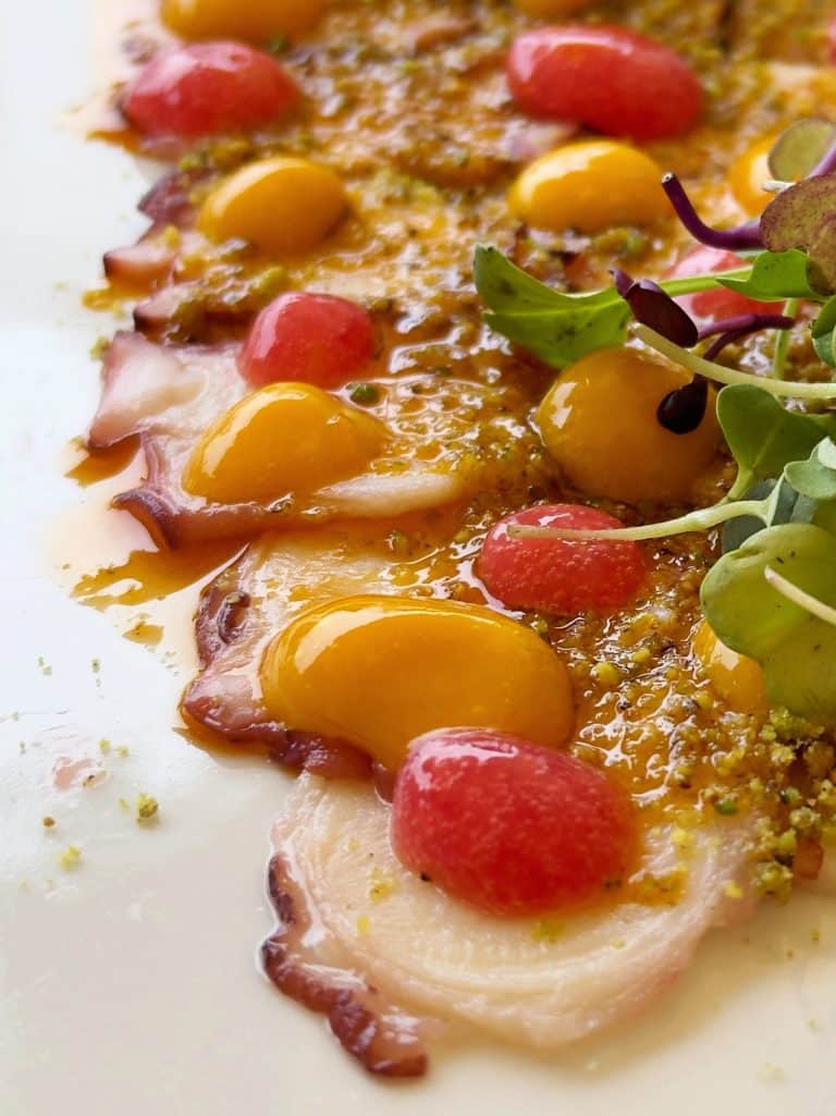 Thinly sliced octopus carpaccio topped with yellow and red sauce drops, green microgreens, and finely ground seasoning—perfect for savoring during your granada 2 day itinerary.