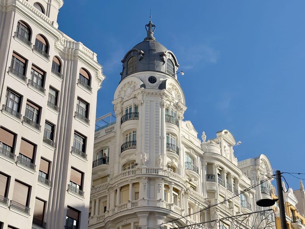 A white ornate historic building with balconies and a rounded tower topped by a dome, set against a clear blue sky on Gran Vía. Power lines are visible in the foreground—one of many architectural highlights among the things to do in Madrid.