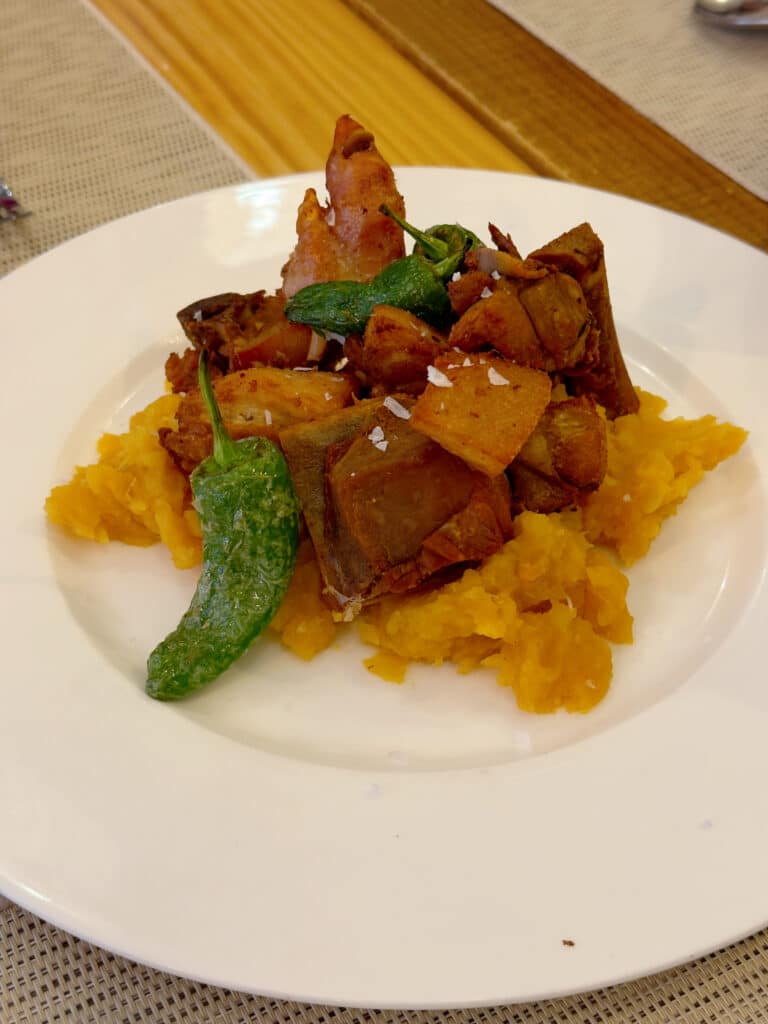 A white plate with a serving of mashed sweet potatoes topped with roasted vegetables, including eggplant and green peppers, garnished with a sprinkle of salt.