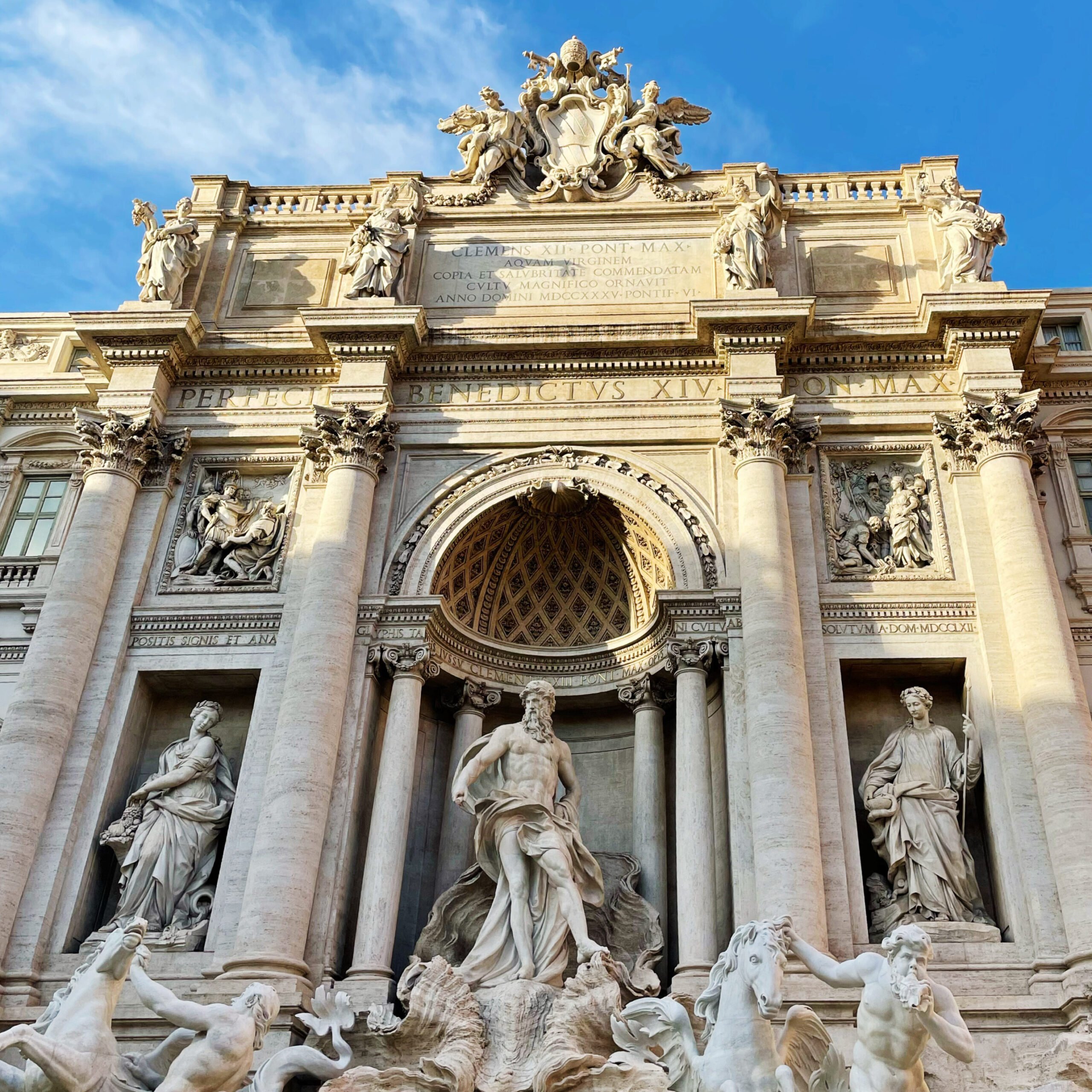 The Trevi Fountain in Rome, Italy, is a must-see on any 3 days in Rome itinerary, featuring elaborate Baroque sculptures, tall columns, and cascading water beneath a blue sky. The central statue depicts Oceanus surrounded by mythological figures.