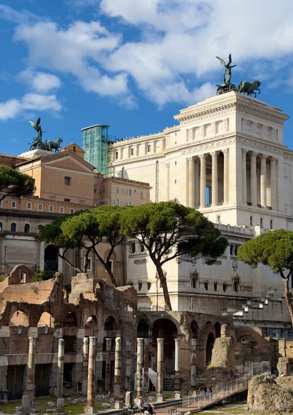 Ancient Roman ruins with stone columns and arches in the foreground, set against the white Altare della Patria monument—an iconic sight you’ll encounter on your 2 days in Rome itinerary beneath a vibrant blue sky.