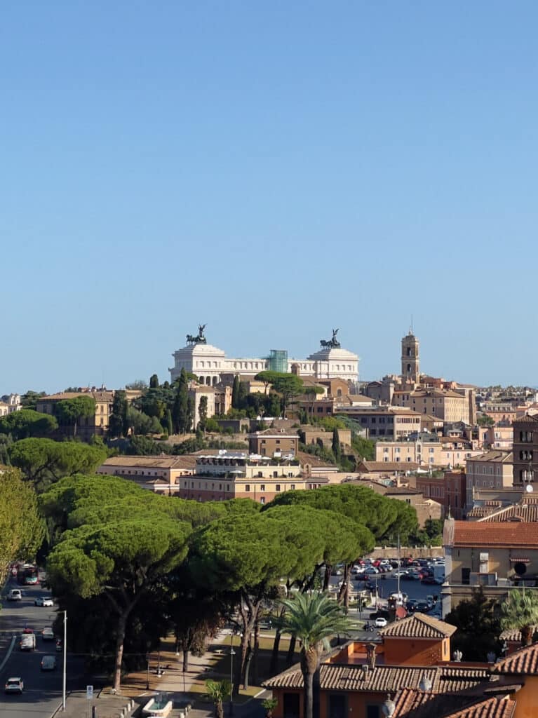 View of Rome with the Altare della Patria monument in the background, surrounded by historic buildings and green trees—an iconic scene perfect for your 3 days in Rome itinerary as cars travel along the bustling streets.