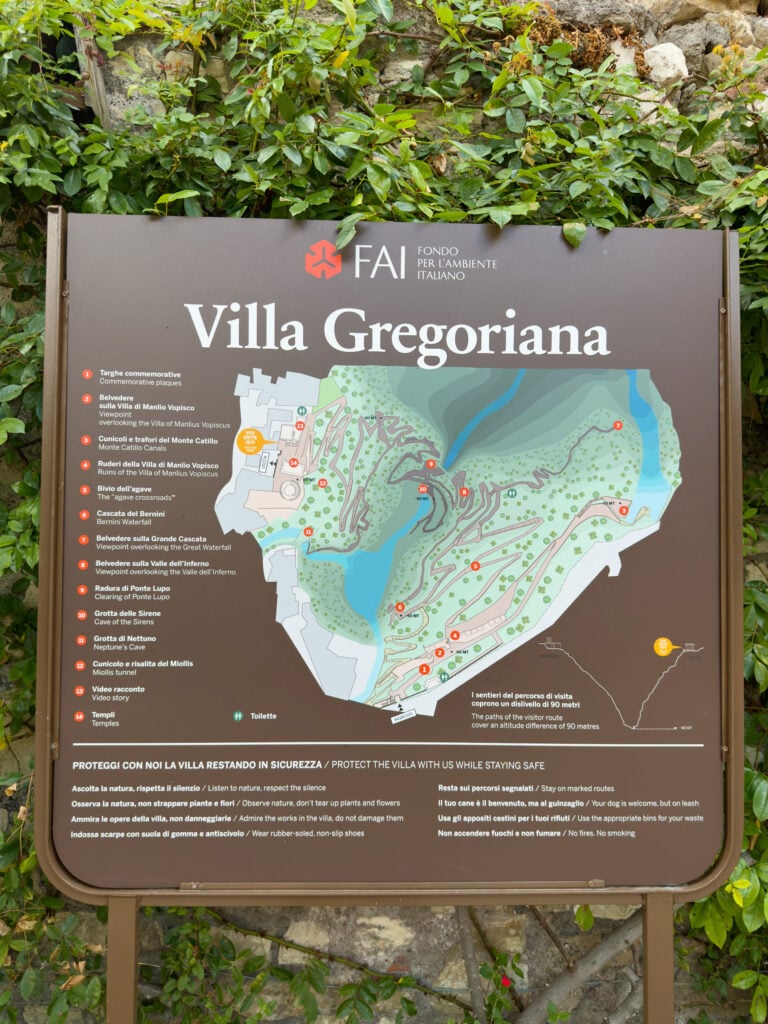 A signboard for Villa Gregoriana with a detailed map of the park, location markers, Italian and English text, and surrounded by leafy green vines.