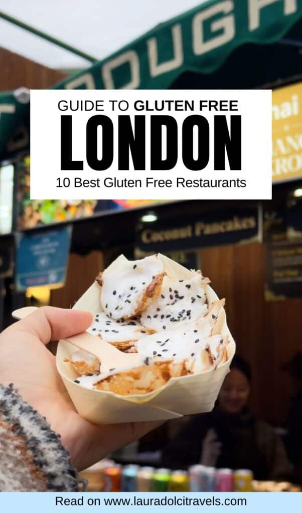 A hand holds gluten-free pancakes topped with white sauce and black sesame seeds at an outdoor market in London. A sign above reads, "Guide to Gluten Free London: 10 Best Gluten Free Restaurants.