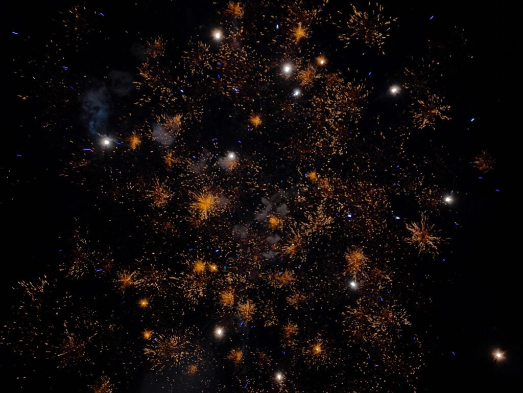 Orange and white fireworks burst against a dark night sky, creating sparkling patterns and scattered bright points of light—a classic scene during November in London.