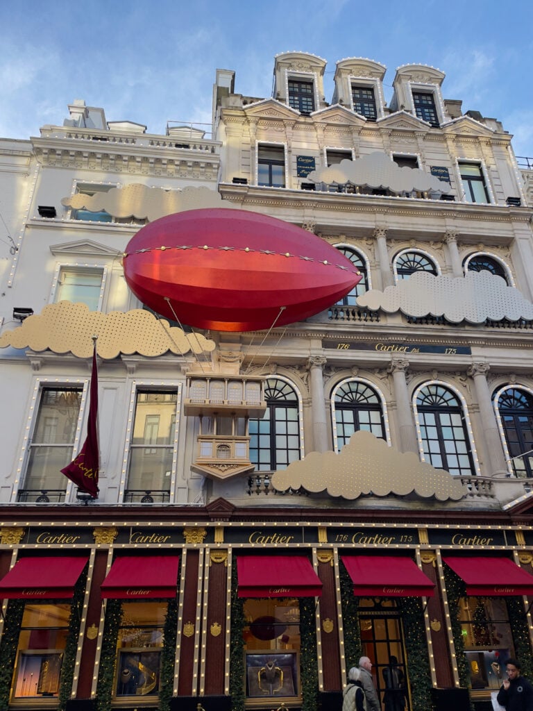 Cartier façade in London decorated with large red balloon floats above a building, clouds, and lights.